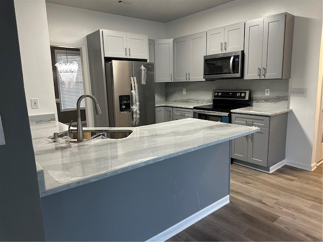 kitchen featuring sink, light stone counters, wood-type flooring, gray cabinets, and stainless steel appliances