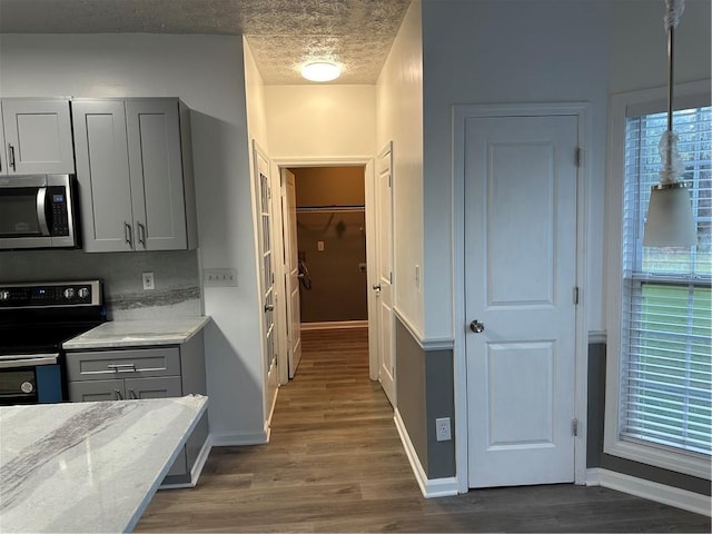 kitchen featuring gray cabinets, appliances with stainless steel finishes, hanging light fixtures, dark hardwood / wood-style floors, and light stone countertops