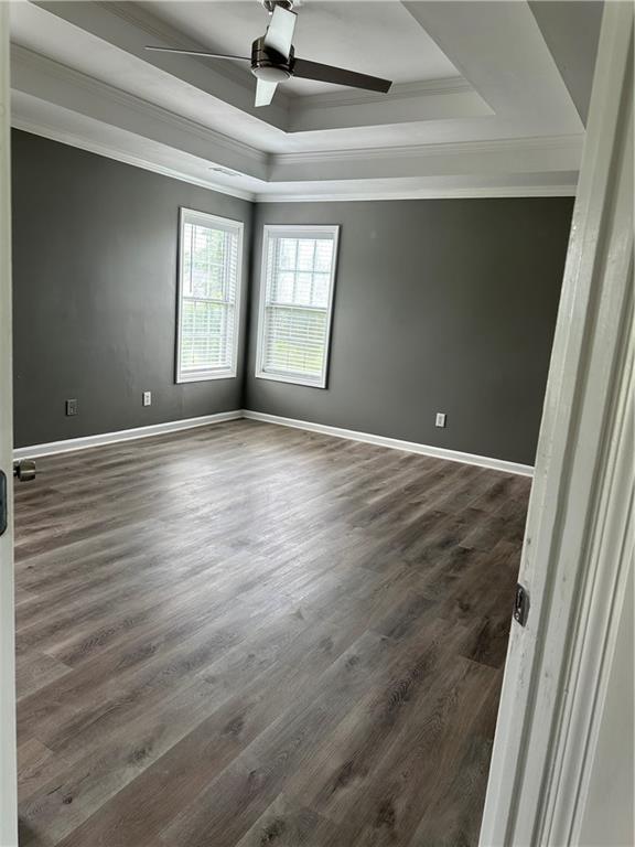 spare room with crown molding, a tray ceiling, dark hardwood / wood-style flooring, and ceiling fan