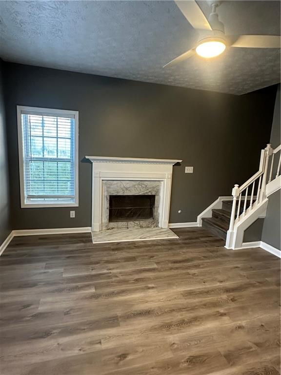 unfurnished living room featuring a premium fireplace, hardwood / wood-style floors, ceiling fan, and a textured ceiling