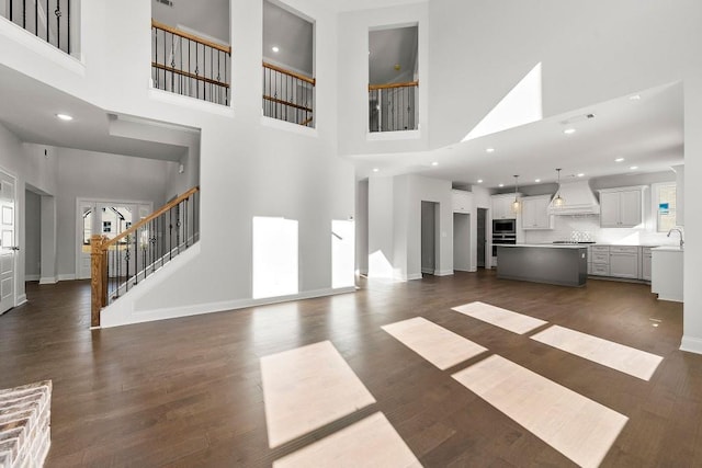 unfurnished living room featuring dark wood-style floors, stairway, a sink, and baseboards