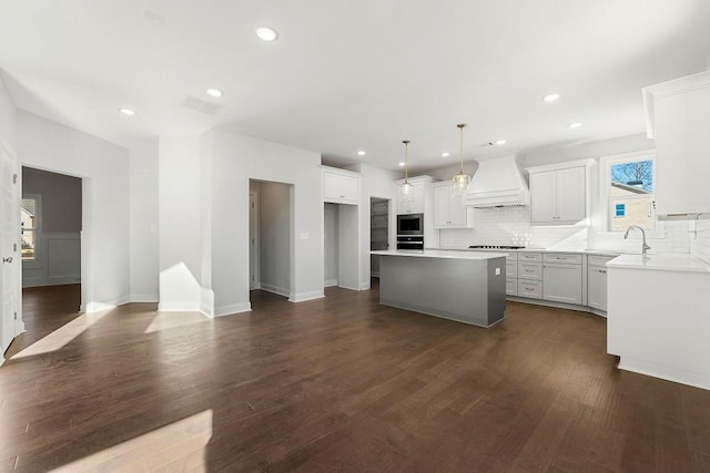 kitchen with white cabinetry, light countertops, custom exhaust hood, a center island, and decorative light fixtures