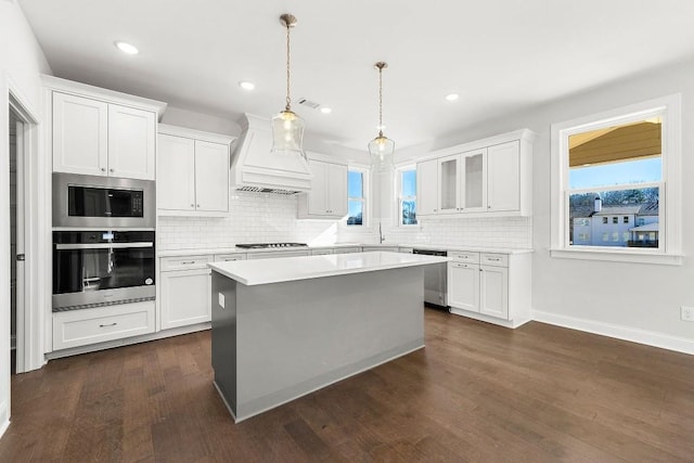 kitchen with appliances with stainless steel finishes, white cabinets, light countertops, and custom range hood