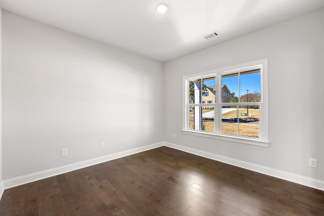 empty room with dark wood-style flooring, visible vents, and baseboards