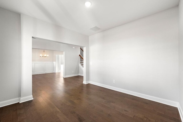 spare room featuring dark wood-style floors, baseboards, stairway, and an inviting chandelier