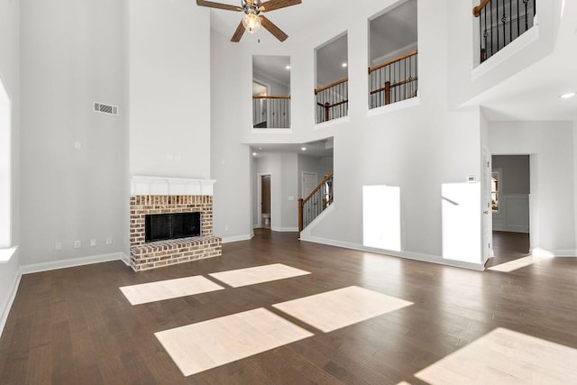 unfurnished living room with dark wood-style flooring, visible vents, baseboards, stairs, and a brick fireplace