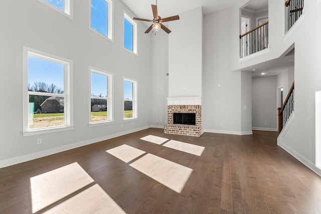 unfurnished living room with a healthy amount of sunlight, a fireplace, stairway, and dark wood-type flooring