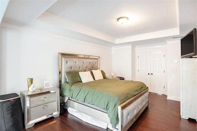 bedroom featuring a tray ceiling, a closet, dark wood-type flooring, and ornamental molding