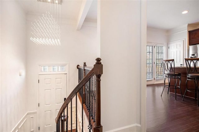 stairway with beamed ceiling, hardwood / wood-style floors, an inviting chandelier, and ornamental molding