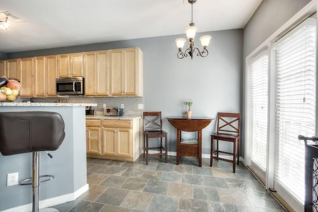 kitchen featuring a healthy amount of sunlight, backsplash, a chandelier, and light stone countertops