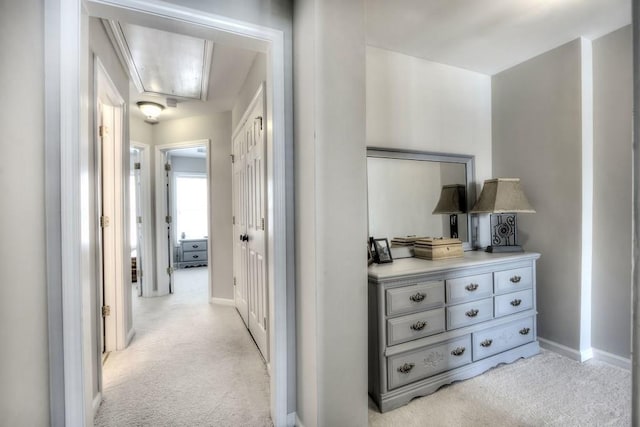 hallway with light carpet, attic access, and baseboards