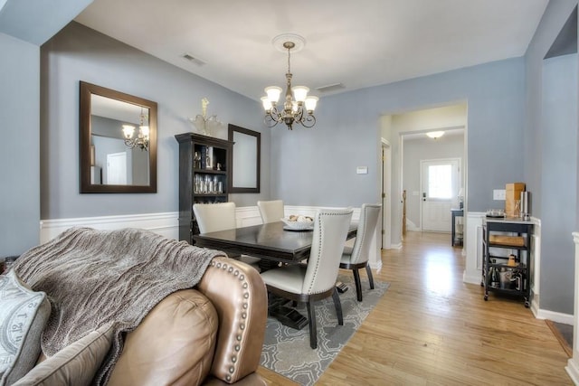 dining space featuring a wainscoted wall, visible vents, light wood finished floors, and an inviting chandelier