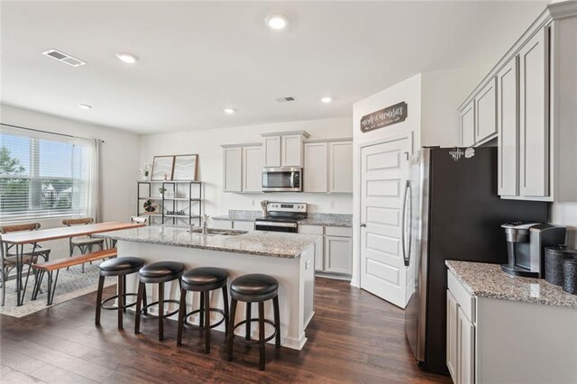 29 Gaston Ct, Hoschton, GA 30548 - kitchen with appliances with stainless steel finishes, dark wood-type flooring, a breakfast bar, gray cabinetry, and a center island with sink