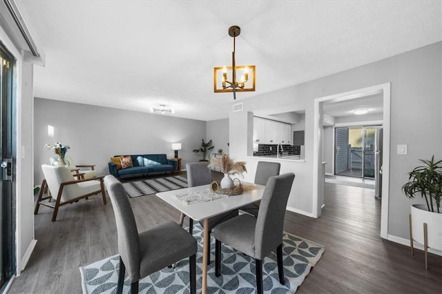 dining space with dark wood-type flooring, a notable chandelier, visible vents, and baseboards