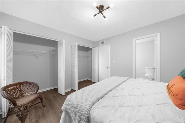 bedroom with multiple closets, ensuite bathroom, dark wood-type flooring, and a textured ceiling