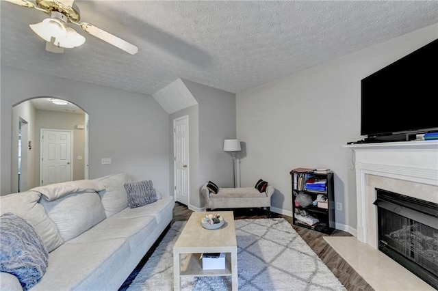 living room with a high end fireplace, a textured ceiling, wood-type flooring, lofted ceiling, and ceiling fan