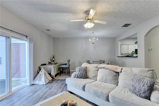 living room with ceiling fan with notable chandelier, a textured ceiling, light wood-type flooring, and plenty of natural light