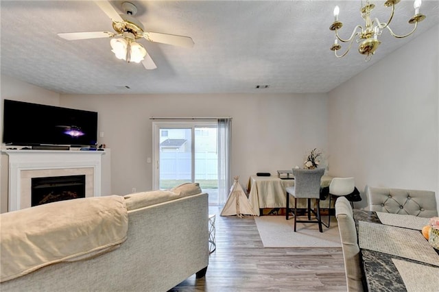 living room featuring hardwood / wood-style flooring, ceiling fan with notable chandelier, and a textured ceiling