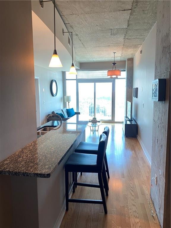 kitchen with decorative light fixtures, a kitchen bar, sink, dark stone countertops, and light hardwood / wood-style flooring