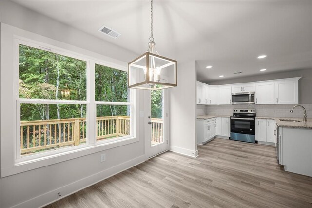 kitchen featuring sink, stainless steel appliances, light stone counters, pendant lighting, and white cabinets