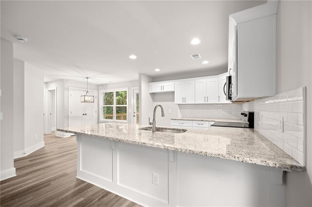 kitchen with stove, kitchen peninsula, sink, tasteful backsplash, and white cabinetry