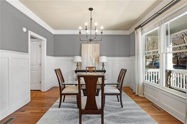 1604 Gilstrap Ln NW, Atlanta, GA 30318 - dining room featuring a chandelier, a decorative wall, wood finished floors, wainscoting, and ornamental molding