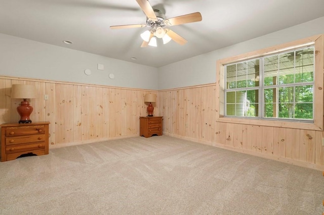 carpeted spare room featuring wood walls and ceiling fan