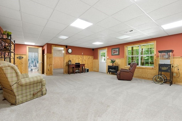 carpeted living room with a drop ceiling and wooden walls