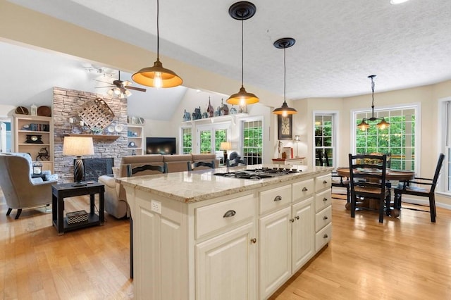 kitchen with light wood-type flooring, hanging light fixtures, ceiling fan, and a center island