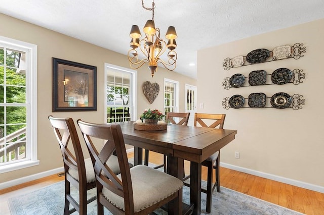 dining area featuring light hardwood / wood-style flooring, a textured ceiling, and an inviting chandelier