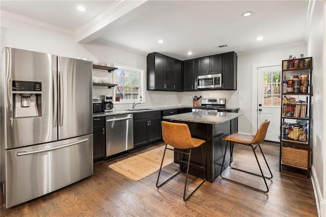 kitchen with dark cabinetry, light stone countertops, a sink, dark wood-type flooring, and appliances with stainless steel finishes