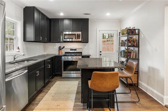 kitchen featuring visible vents, a kitchen island, dark stone counters, ornamental molding, and stainless steel appliances