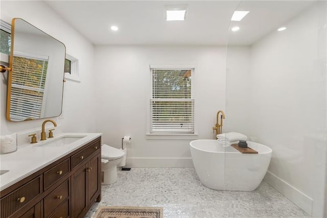 full bath featuring baseboards, double vanity, a freestanding bath, a sink, and toilet