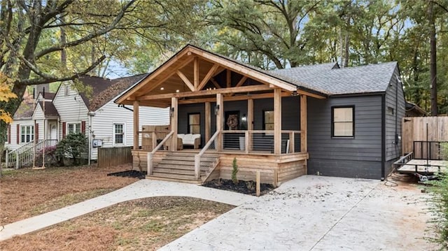 bungalow-style home featuring covered porch, a shingled roof, and fence