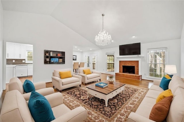 living area with a notable chandelier, a fireplace, light wood finished floors, recessed lighting, and high vaulted ceiling