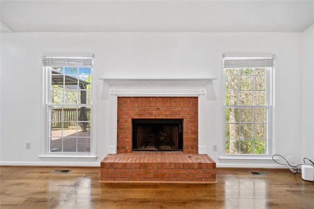 unfurnished living room with a fireplace, visible vents, baseboards, and wood finished floors