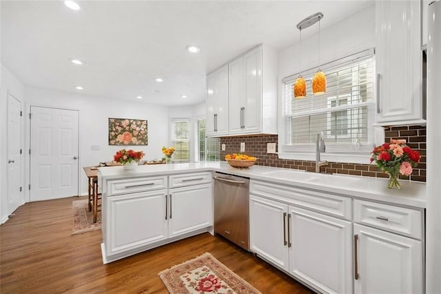 kitchen with a peninsula, dishwasher, a sink, and dark wood-style flooring