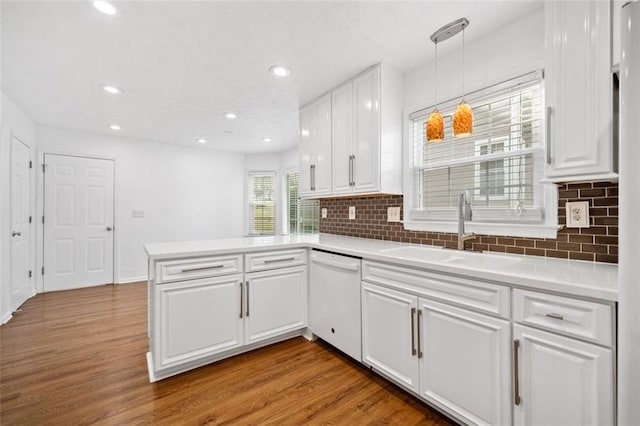 kitchen with a peninsula, white cabinetry, dishwasher, a sink, and wood finished floors
