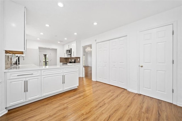 kitchen featuring white cabinets, a sink, light wood finished floors, recessed lighting, and stainless steel appliances