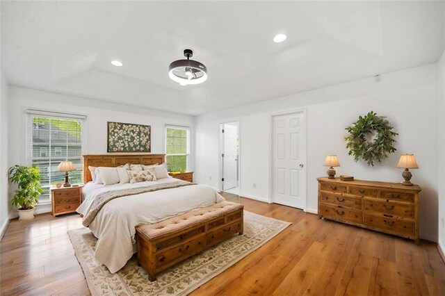 bedroom featuring a tray ceiling, light wood-style floors, multiple windows, and recessed lighting