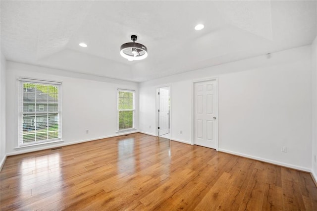 unfurnished room with a tray ceiling, wood finished floors, baseboards, and visible vents