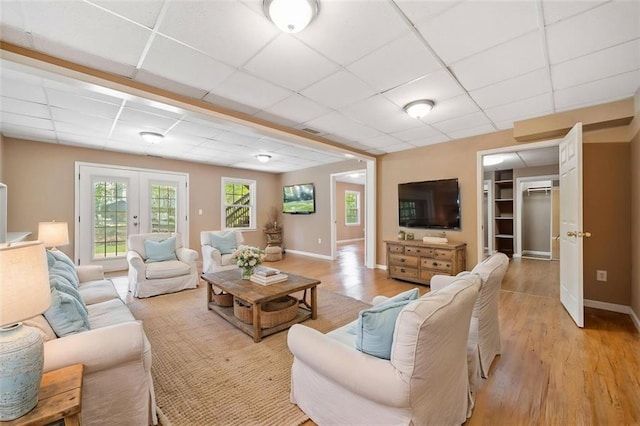 living area featuring light wood-style flooring, french doors, and a drop ceiling