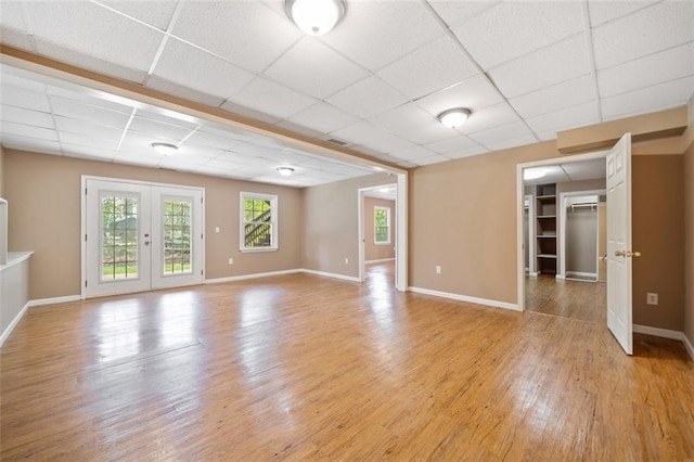 unfurnished living room with baseboards, a drop ceiling, and light wood-style floors