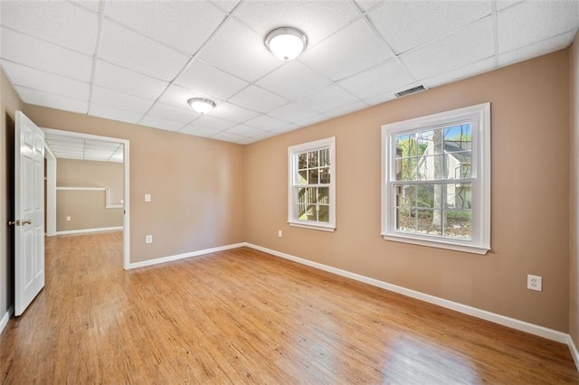 empty room featuring visible vents, light wood-style flooring, a drop ceiling, and baseboards