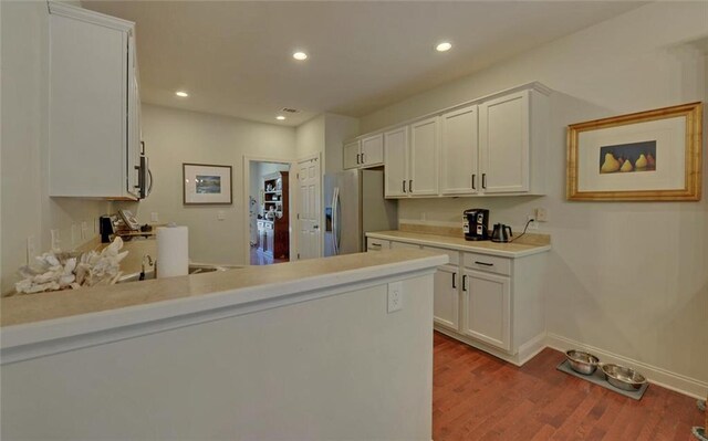 kitchen featuring stainless steel appliances, light wood-type flooring, kitchen peninsula, and white cabinetry