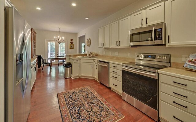 kitchen featuring hanging light fixtures, kitchen peninsula, stainless steel appliances, light wood-type flooring, and an inviting chandelier