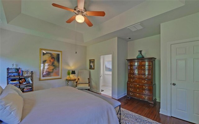 bedroom with ceiling fan, a raised ceiling, ensuite bathroom, and dark wood-type flooring