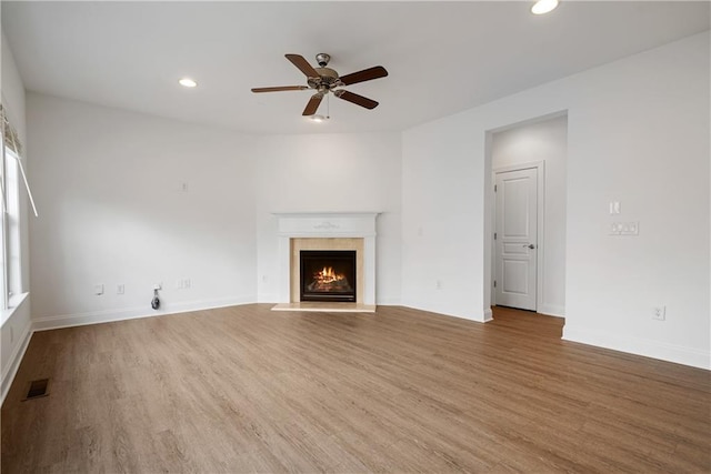 unfurnished living room featuring a ceiling fan, wood finished floors, recessed lighting, a lit fireplace, and baseboards