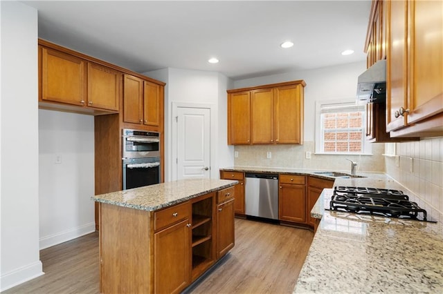 kitchen with light wood-type flooring, light stone counters, brown cabinetry, stainless steel appliances, and a sink