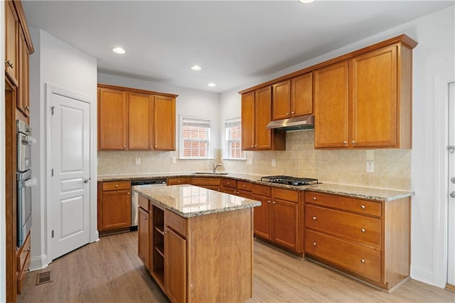 kitchen featuring under cabinet range hood, brown cabinets, stainless steel appliances, and light wood-style flooring